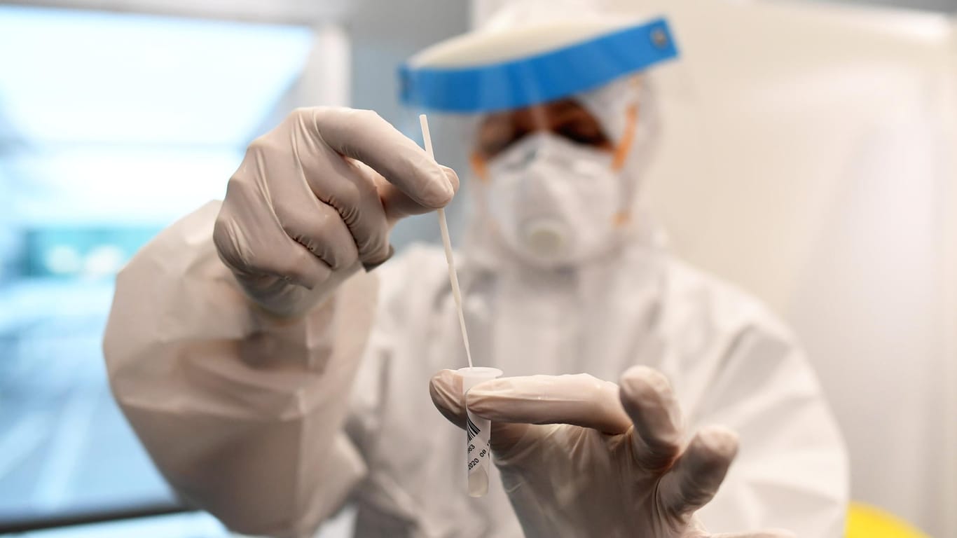 Ein Mitarbeiter eines Testcenters hält eine Abstrich-Probe in der Hand (Archivbild). In Deutschland sinken die Infektionszahlen.