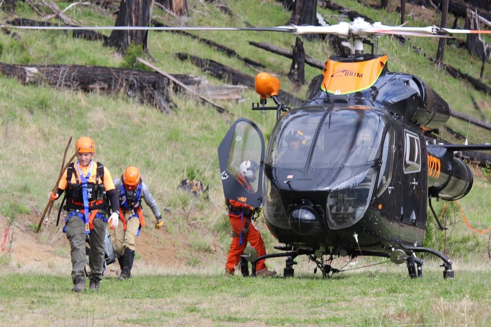 Rettungskräfte vor einem Helikopter: Suchtrupps hinterließen Nahrung und kleine Botschaften an den Waldwegen.