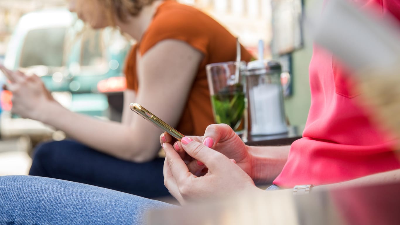 Smartphone-Nutzerinnen im Freien: Ganz sicher unsicher ist es, im offenen WLAN eines Cafés zu surfen. Abhilfe schaffen hier VPN-Dienste oder das Internet über den Mobilfunk.