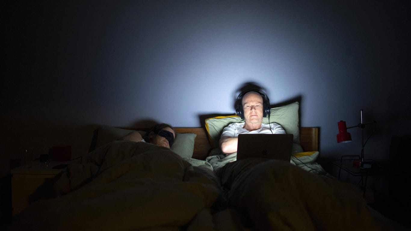 Ein Mann liegt mit seinem Laptop im Bett (Symbolbild): Wer bis spät arbeitet, schläft meist schlechter.