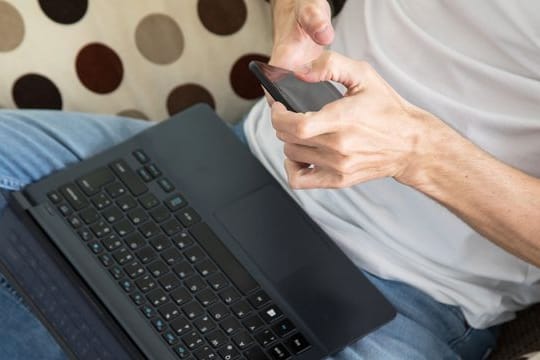An Mann liest neue Nachrichten auf dem Smartphone: Meldet sich angeblich der Zoll per E-Mail, ist erst einmal höchste Skepsis angebracht – vor allem wenn eine Prepaid-Zahlung gefordert wird.