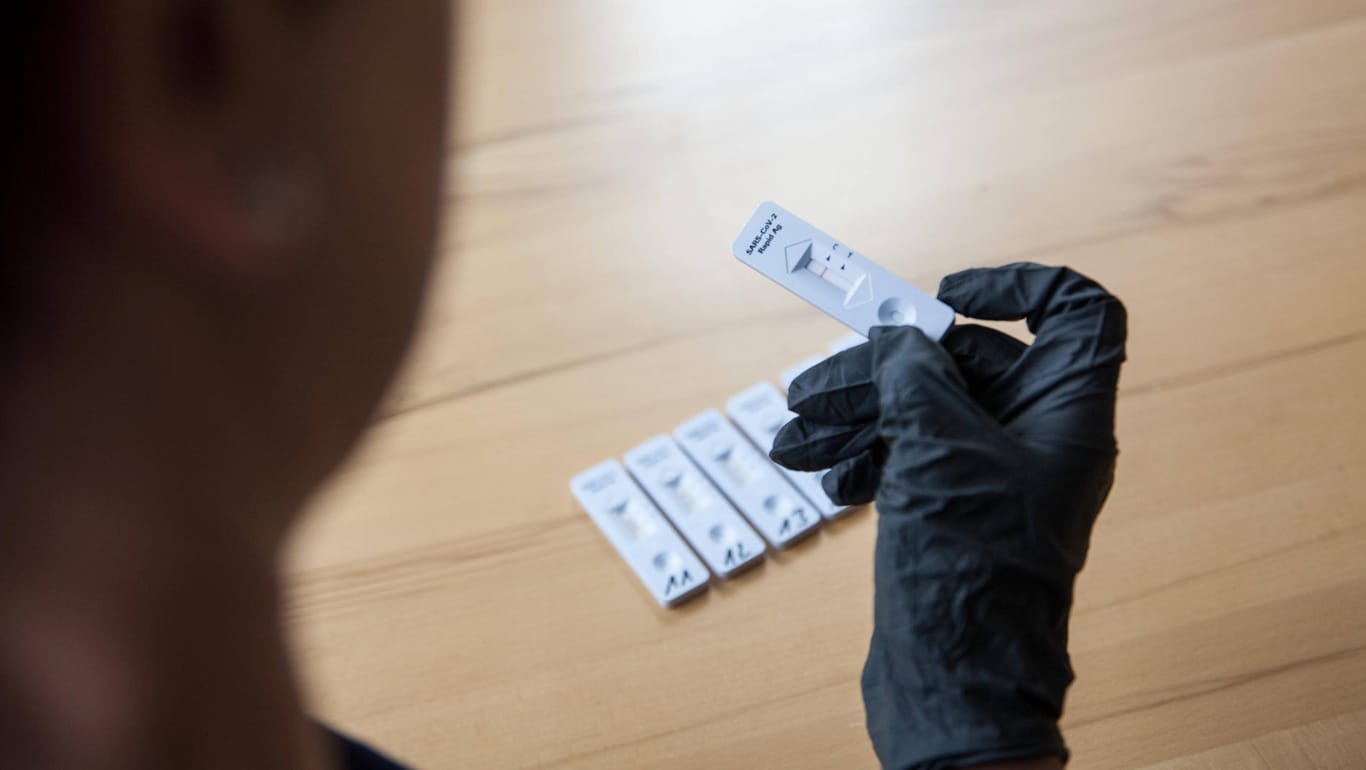 Person mit Schutzhandschuhen blickt auf einen Antigen-Test (Symbolbild): In mehreren Bundesländern wird wegen möglichem Betrug um Corona-Testzentren ermittelt.