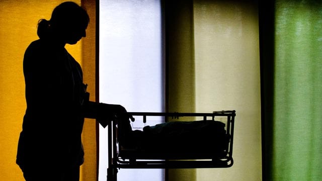 Eine Hebamme schiebt in einer Geburtsstation einen Wagen mit einem Baby.