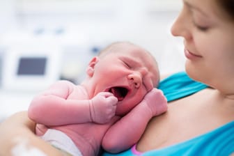 Junge Frau hält ihr Neugeborenes im Arm.