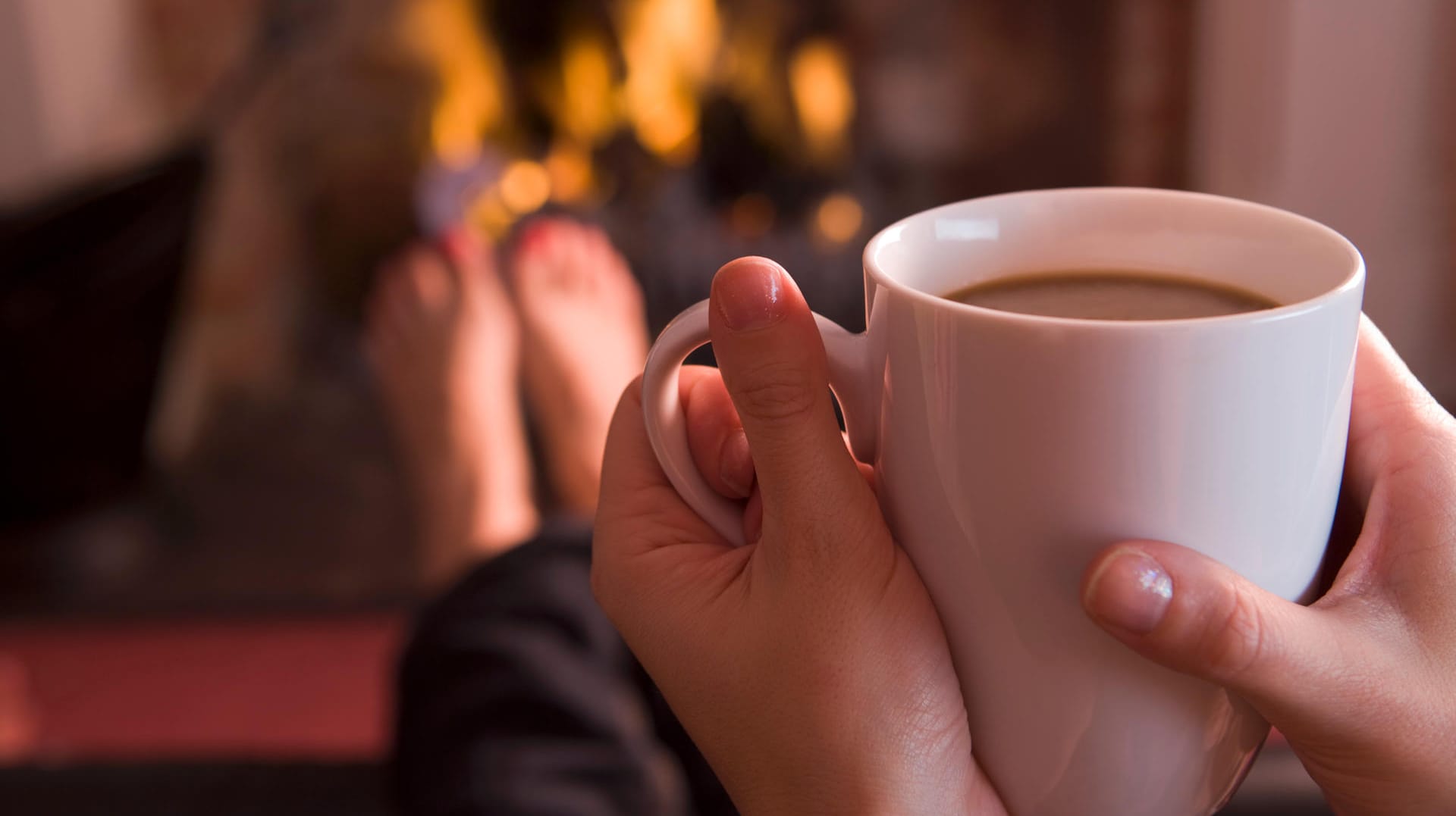 Eine Frau sitzt vor dem Kamin und trinkt Kaffee