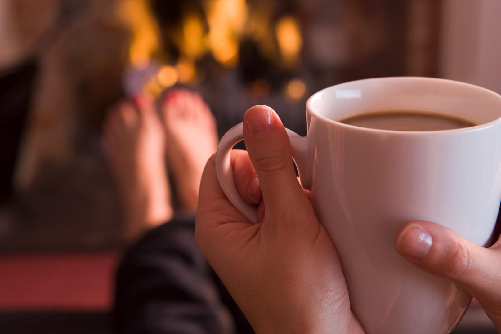 Eine Frau sitzt vor dem Kamin und trinkt Kaffee