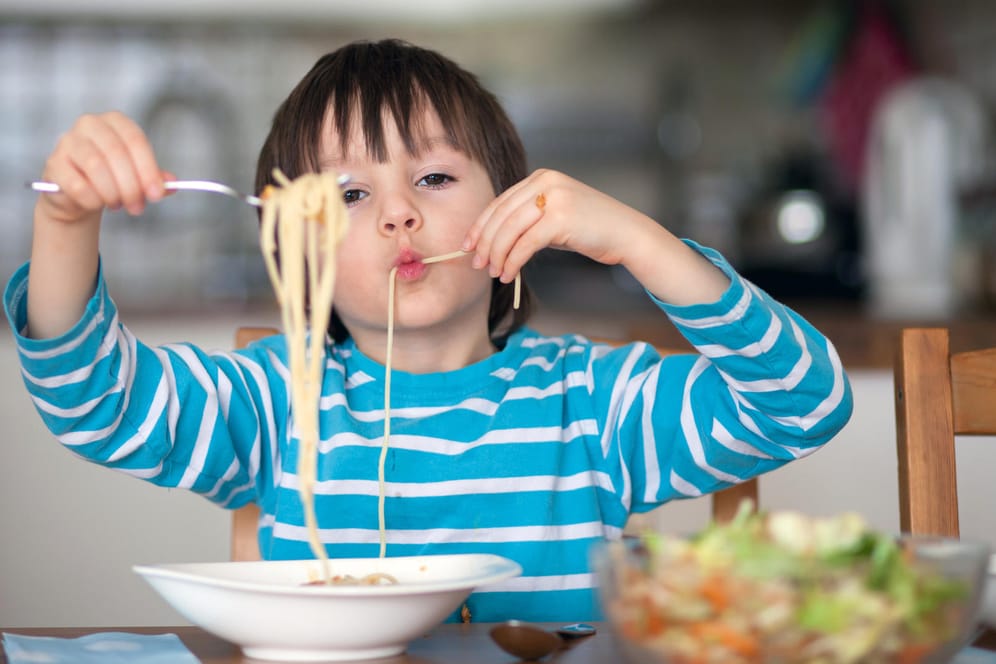 Ein Junge isst Spaghetti: Warum man nicht mit Essen spielt, müssen Kinder erst verstehen.