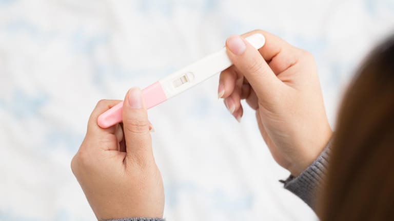 Eine Frau hält einen positiven Schwangerschaftstest in den Händen
