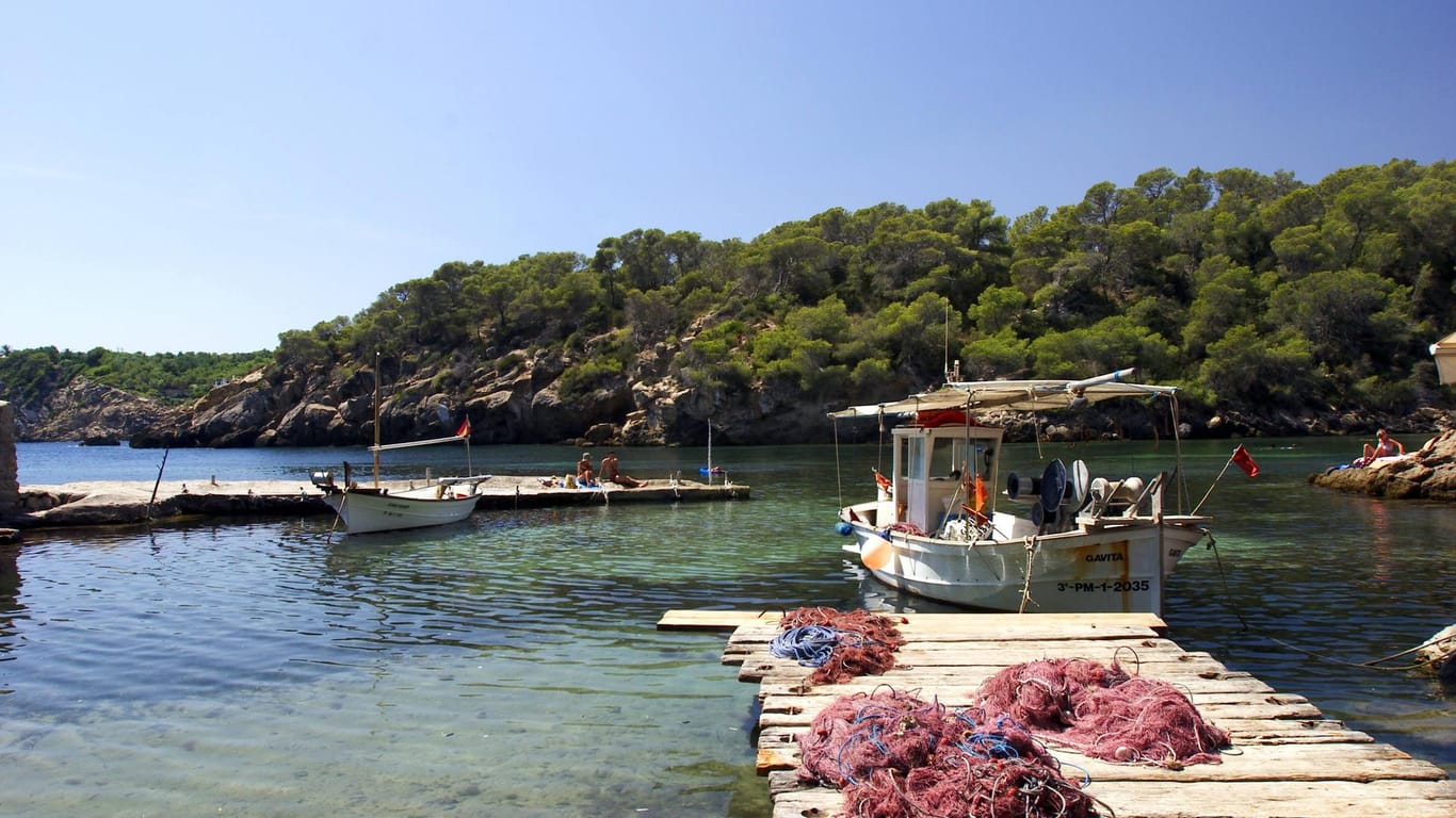Cala Mastella: In der kleinen Bucht liegen Fischerboote. Auf den Stegen sonnen sich Urlauber.