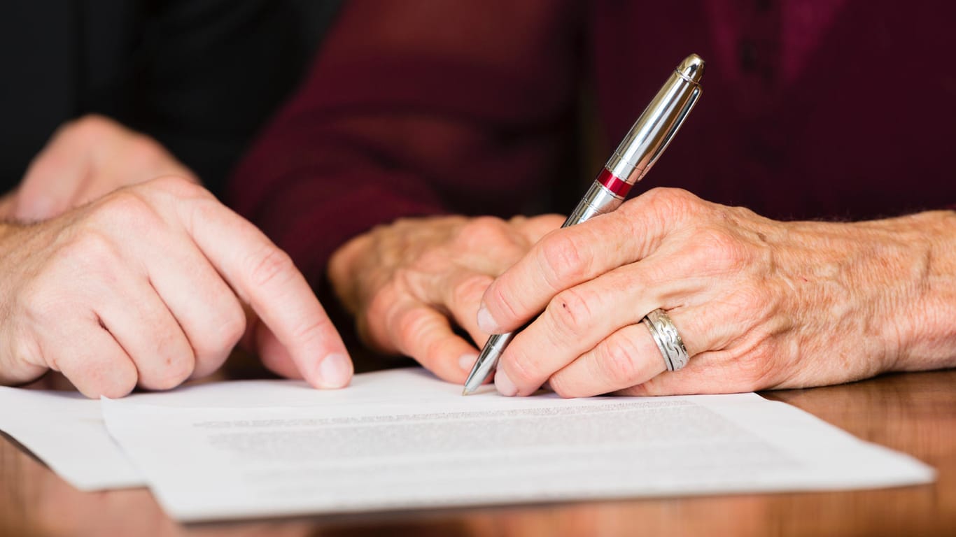 Ältere Frau unterzeichnet ein Dokument: Das Erbrecht garantiert auch ungeliebten Kindern und Verwandten einen Pflichtteil am Nachlass.