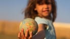 Kind hält einen Globus in der Hand.