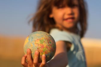 Kind hält einen Globus in der Hand.