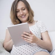 Schwangere Frau mit Tablet: Mutterschaftsgeld können werdende Mütter bequem online beantragen.