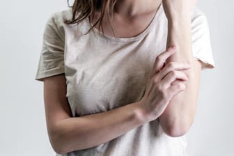 Frau kratzt sich den Arm: Schuppenflechte ist eine häufig auftretende, entzündliche Hautkrankheit.