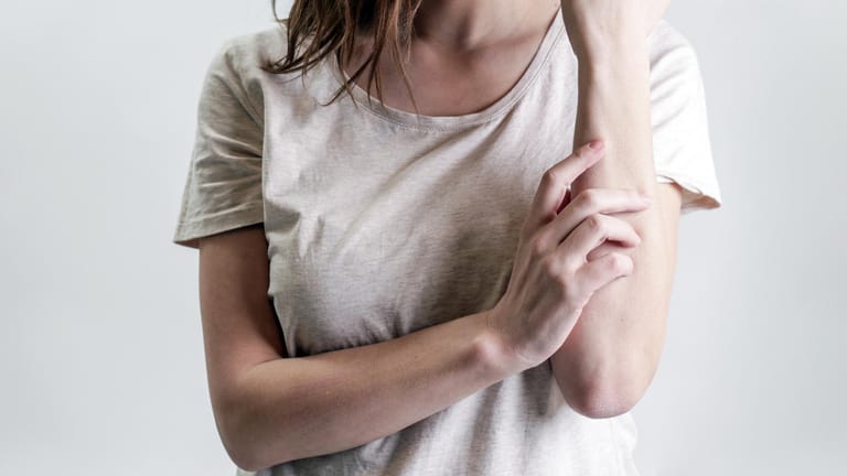 Frau kratzt sich den Arm: Schuppenflechte ist eine häufig auftretende, entzündliche Hautkrankheit.