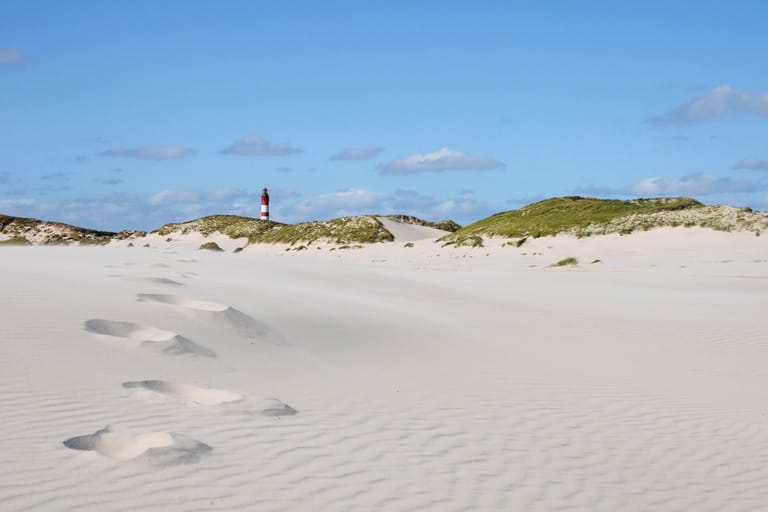 Amrum: Mit Spuren im feinen Sand und dem Leuchtturm im Hintergrund kommt maritimes Urlaubes-Feeling auf.
