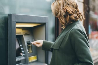 Eine Frau nutzt einen Geldautomaten (Symbolbild): Wer Bargeld abheben möchte, benötigt dafür ein eigenes Konto.