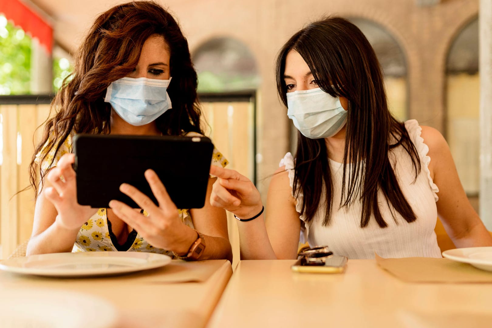 Zwei junge Frauen bedienen ein Tablet in einem Restaurant: Der CCC zeigt Sicherheitslücken bei Dienstleistern für "Corona-Listen".