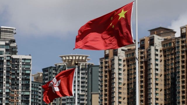 Die Flagge der Sonderverwaltungszone Hongkong (l) und die Flagge der Volksrepublik China wehen vor Wolkenkratzern. Die Flagge der Sonderverwaltungszone Hongkong (l) und die Flagge der Volksrepublik China wehen vor Wolkenkratzern.
