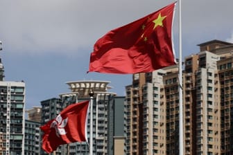 Die Flagge der Sonderverwaltungszone Hongkong (l) und die Flagge der Volksrepublik China wehen vor Wolkenkratzern.
