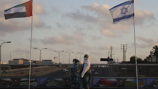 Frauen mit Schutzmasken gehen an den Flaggen von Israel und den Vereinigten Arabischen Emiraten auf der Friedensbrücke im israelischen Netanya vorbei.