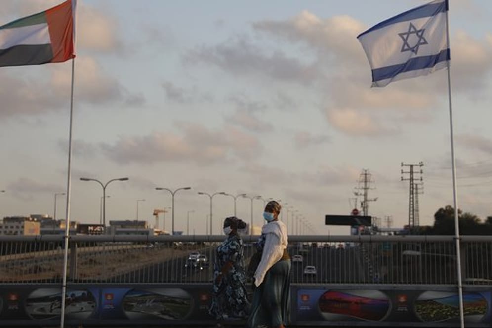 Frauen mit Schutzmasken gehen an den Flaggen von Israel und den Vereinigten Arabischen Emiraten auf der Friedensbrücke im israelischen Netanya vorbei.