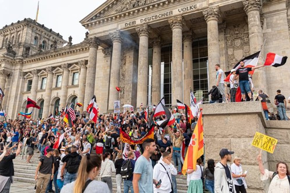 Teilnehmer einer Kundgebung gegen die Corona-Maßnahmen stehen auf den Stufen zum Reichstagsgebäude, zahlreiche Reichsflaggen sind zu sehen.