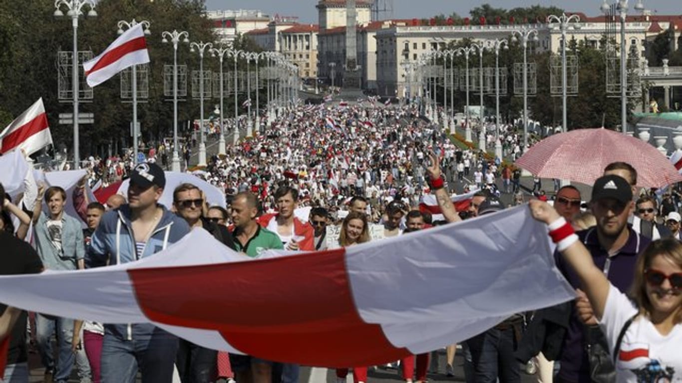 Demonstranten marschieren mit der ehemaligen belarussischen Nationalflagge in den Händen auf der Straße.
