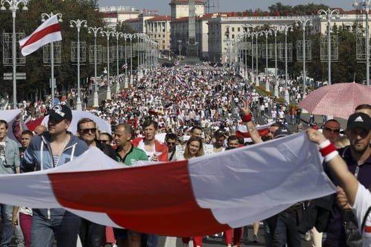 Demonstranten marschieren mit der ehemaligen belarussischen Nationalflagge in den Händen auf der Straße.