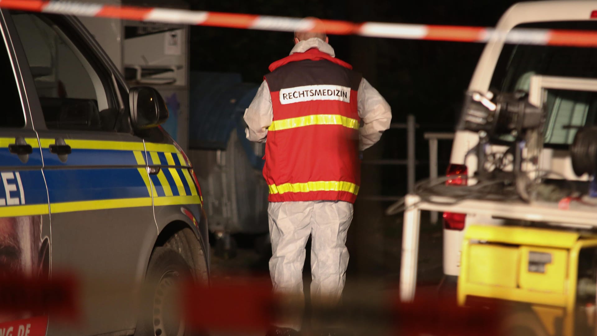 Ein Rechtsmediziner geht zwischen zwei Polizeifahrzeugen durch: Am Abend war ein Mann mit tödlichen Schussverletzungen gefunden worden.