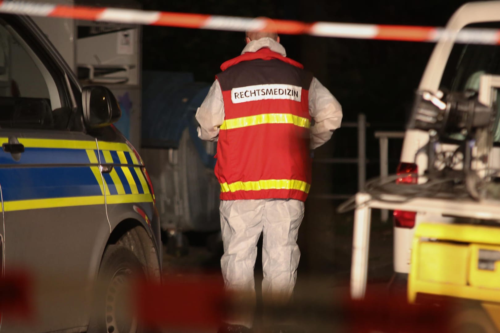 Ein Rechtsmediziner geht zwischen zwei Polizeifahrzeugen durch: Am Abend war ein Mann mit tödlichen Schussverletzungen gefunden worden.