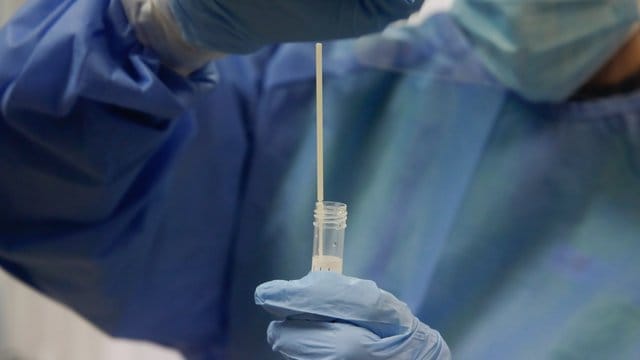 Ein medizinischer Mitarbeiter hält in einem Testzentrum einen Abstrich. Ein medizinischer Mitarbeiter hält in einem Testzentrum einen Abstrich.