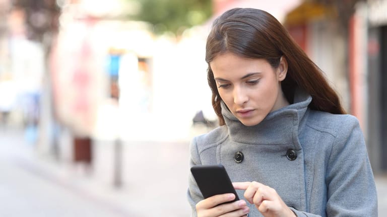 Eine Frau schaut auf ihr Smartphone (Symbolbild): Spam-Nummern können Sie blocken.