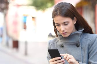Eine Frau schaut auf ihr Smartphone (Symbolbild): Spam-Nummern können Sie blocken.
