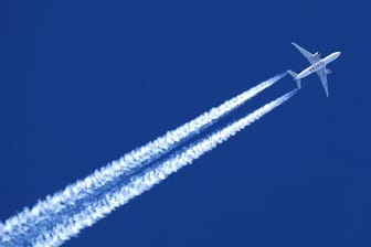 Ein Flugzeug hinterlässt Kondensstreifen am wolkenlosem Himmel.