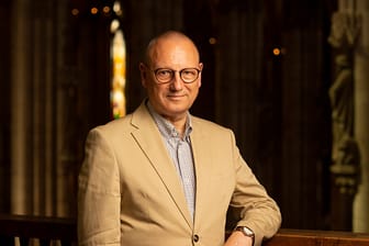 Chorleiter Wolfgang Spieler lehnt am Geländer einer Kirche: Er leitet seit fast 40 Jahren den "reger chor köln" und wird dafür nun ausgezeichnet.