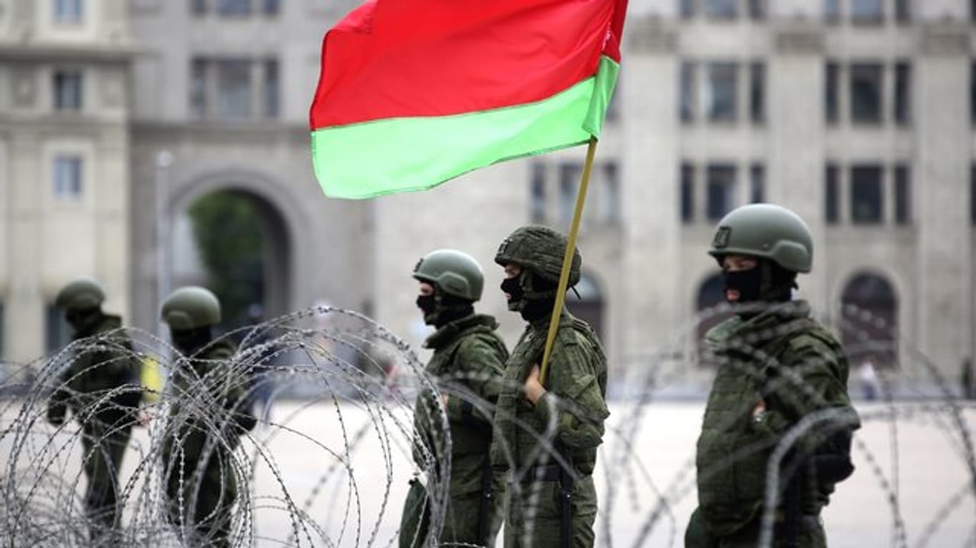 Uniformierte Sicherheitskräfte stehen in Minsk mit der belarussischen Staatsflagge hinter Stacheldraht.