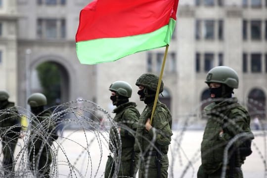 Uniformierte Sicherheitskräfte stehen in Minsk mit der belarussischen Staatsflagge hinter Stacheldraht.