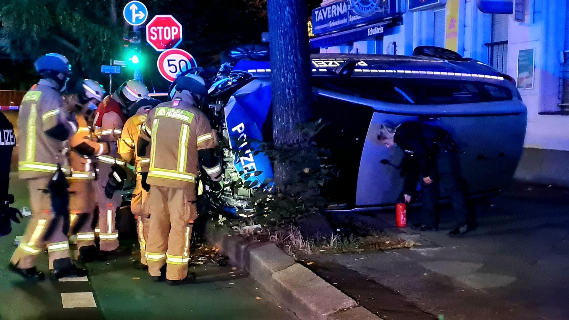 Einsatzkräfte stehen an einem Polizeifahrzeug: Der Einsatzwagen ist bei einem Unfall während einer Verfolgungsjagd gegen einen Baum geprallt.