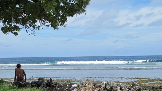 Ein Junge sitzt am Sandstrand auf der Fidschi-Insel Kiribati neben Abfällen. Ein Junge sitzt am Sandstrand auf der Fidschi-Insel Kiribati neben Abfällen.