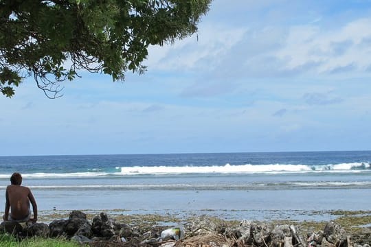 Ein Junge sitzt am Sandstrand auf der Fidschi-Insel Kiribati neben Abfällen.