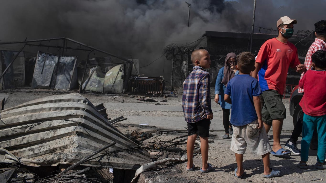 Nahezu komplett verbrannt: Kinder und Erwachsene stehen neben zerstörten Zelten und Containern in Moria.