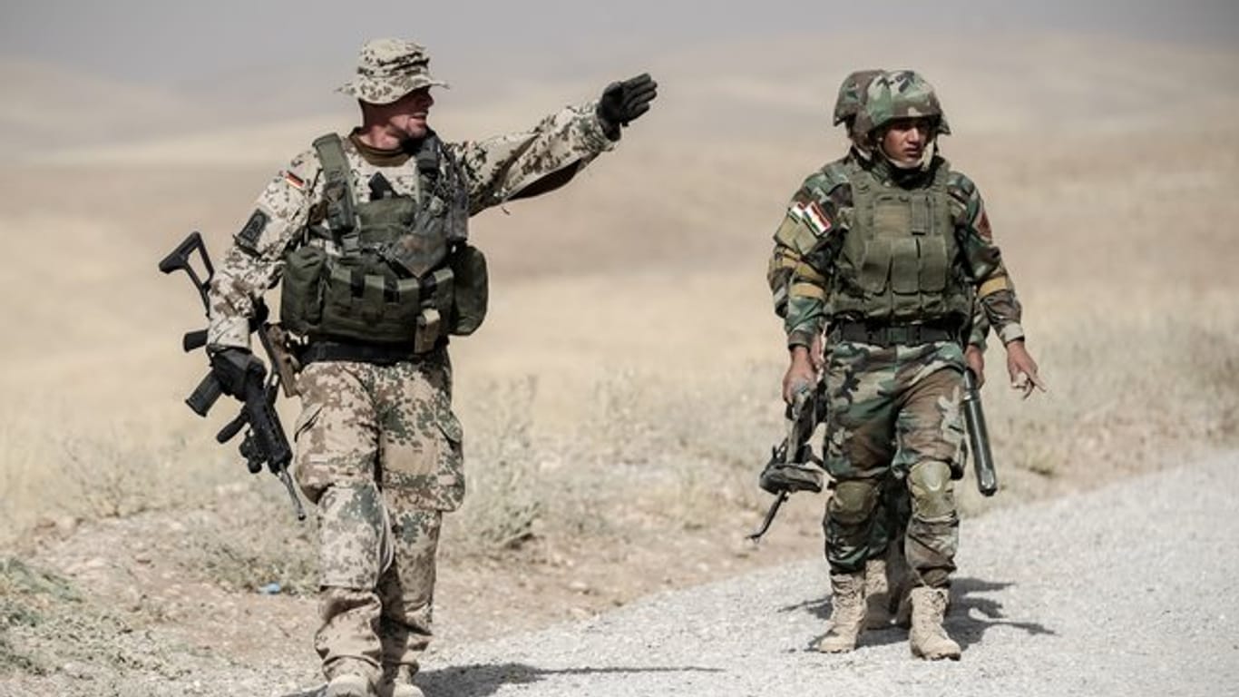 Bundeswehrsoldaten und kurdische Peshmerga Soldaten gehen in der Ausbildungseinrichtung Bnaslawa bei einer Übung am Rand einer Straße in Irak entlang.