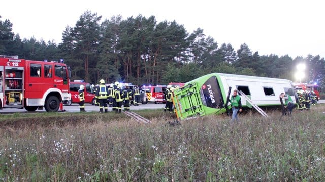 Feuerwehrleute stehen an der Autobahn A24 neben einem verunglückten Fernbus.