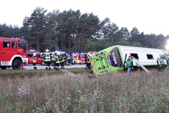 Feuerwehrleute stehen an der Autobahn A24 neben einem verunglückten Fernbus.