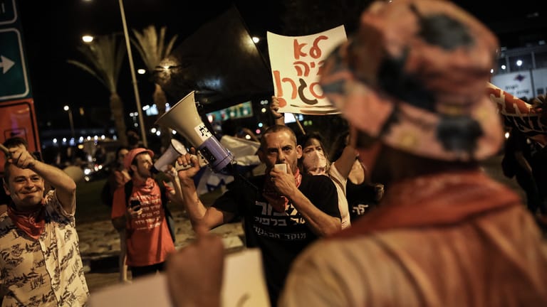Lod: Demonstranten rufen Parolen in ein Megafon bei einem regierungskritischen Protest vor dem Flughafen Ben Gurion vor dem Abflug des israelischen Premierministers Netanjahu in die USA.