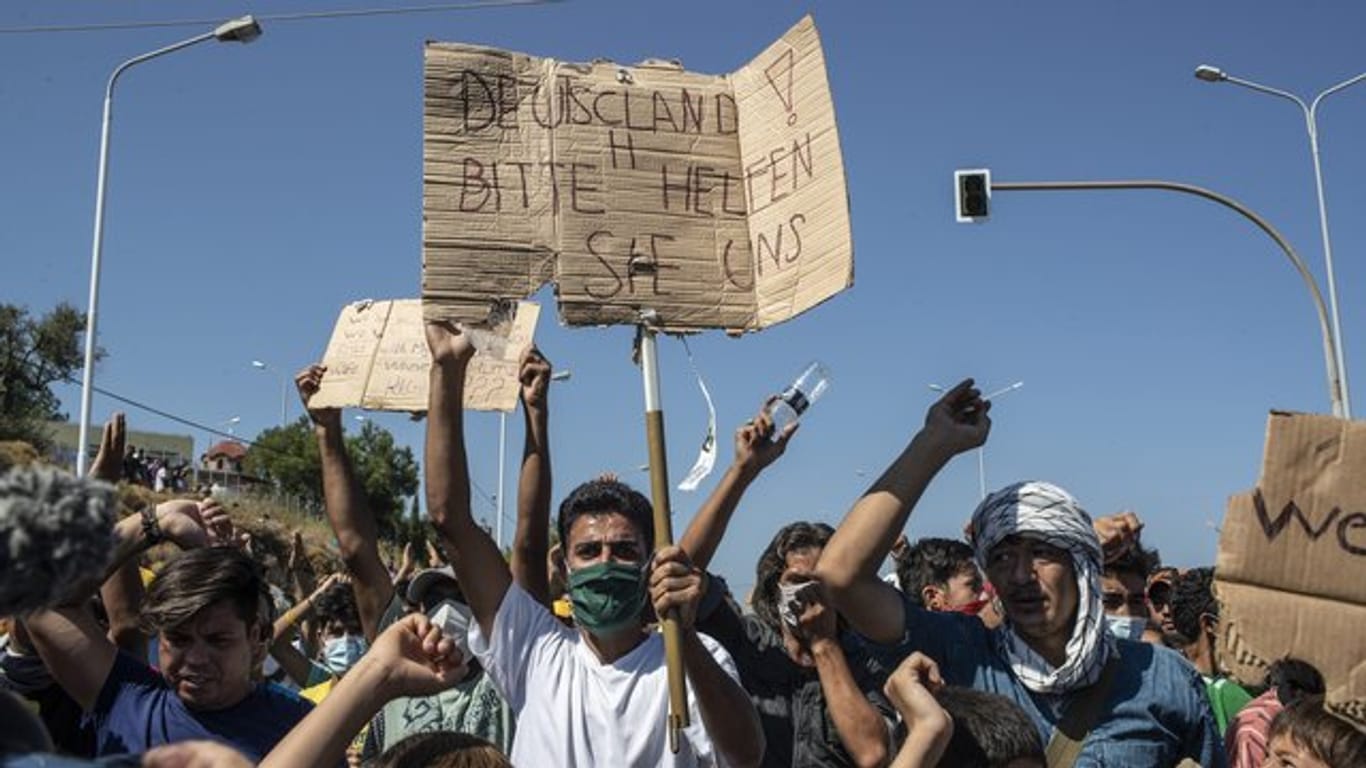 Ein Flüchtling auf Lesbos hält ein Plakat mit der Aufschrift "Deutschland, bitte helfen sie uns".