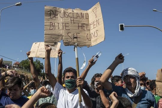 Ein Flüchtling auf Lesbos hält ein Plakat mit der Aufschrift "Deutschland, bitte helfen sie uns".