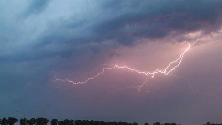 Ein Blitz erhellt den Abendhimmel über einem Feld (Symbolbild): In der Schweiz sind mehrere Jugendliche beim Fußballspielen von einem Unwetter überrascht worden.