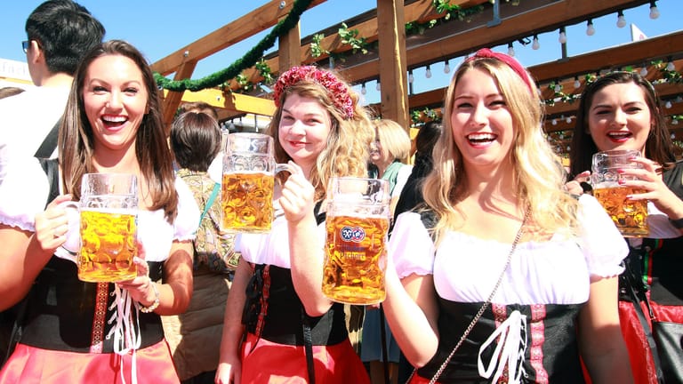 Frauen in einheitlichen Wiesndirndl posieren mit einer Mass Bier in der Hand (Symbolbild): Tracht gehört zum Wiesn-Look.